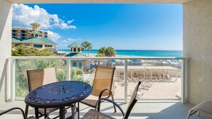 Un balcon avec une table et des chaises, donnant sur une plage et sur les bâtiments d’un hôtel.