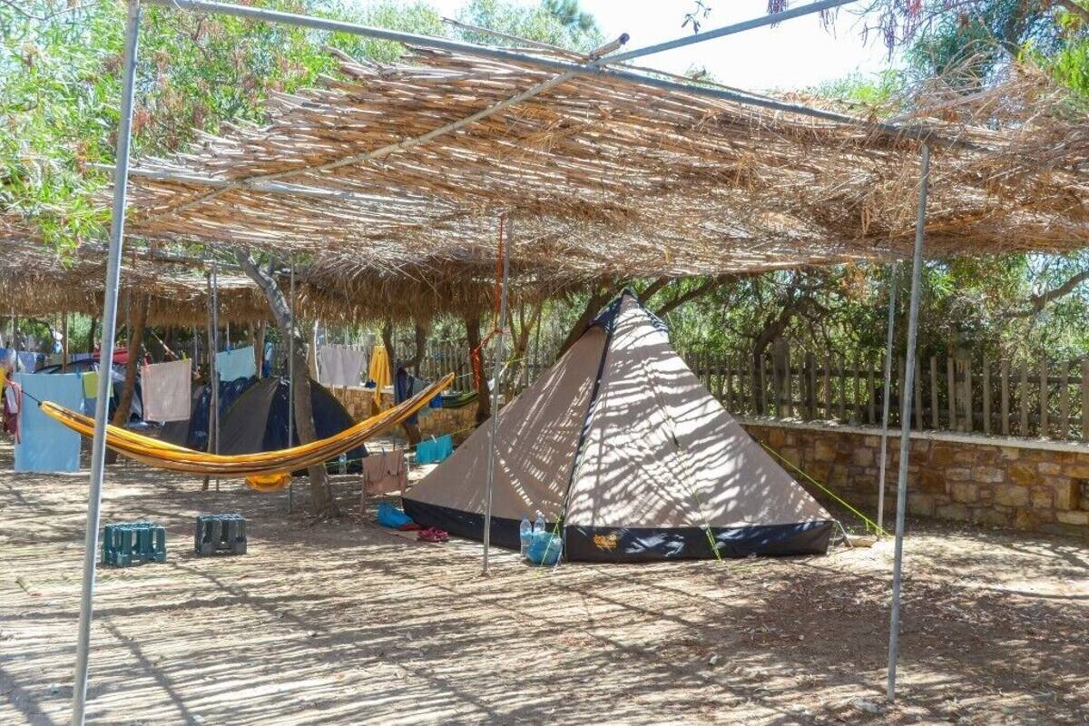A campsite with a large thatched roof structure, a hammock, and a tent.