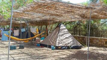 A campsite with a large thatched roof structure, a hammock, and a tent.
