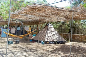 A campsite with a large thatched roof structure, a hammock, and a tent.