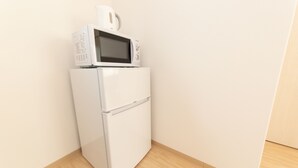 Ein weißer Kühlschrank mit einer Mikrowelle darauf, steht in einer Ecke an einer schlichten Wand.