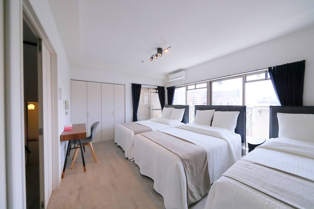 A hotel room with three beds, a desk, and a chair.