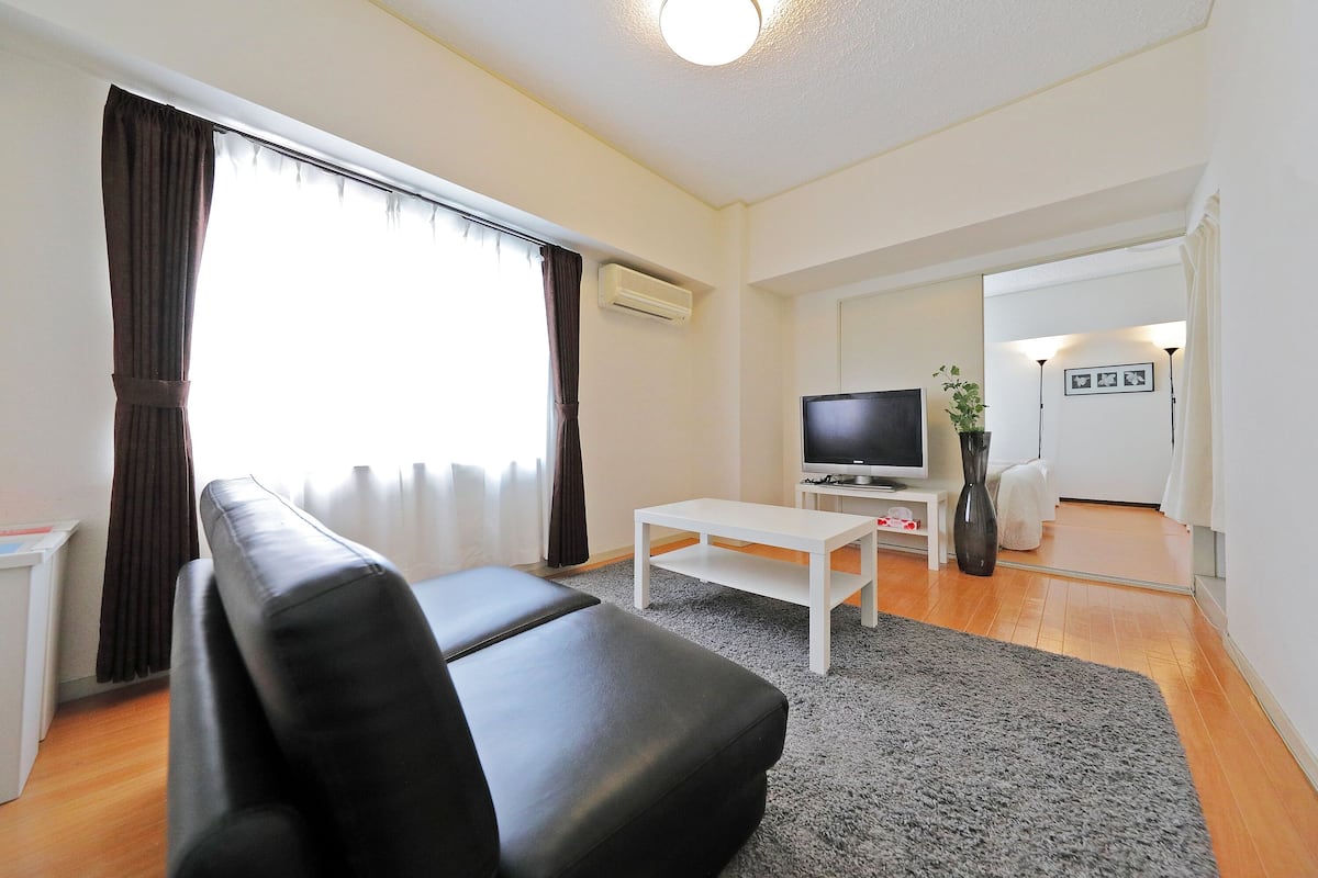 A modern living room with a black leather sofa, a white coffee table, and a flat-screen TV.