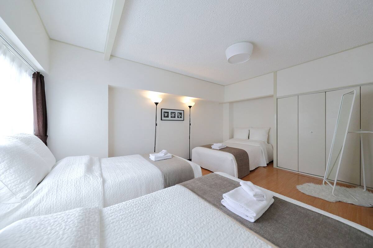 A hotel room with two beds, a wardrobe, a mirror, and a small rug.