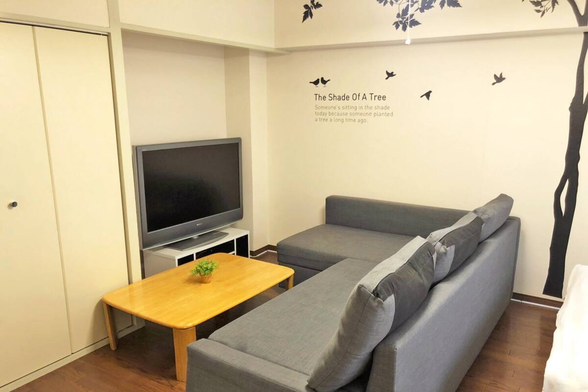 A modern living room with a grey sofa, a wooden coffee table, and a flat-screen TV on a stand.