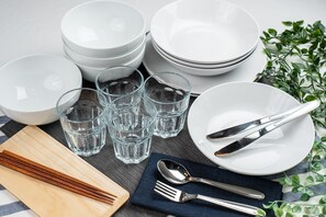 A set of white dinnerware including bowls, plates, and glasses, arranged on a table with chopsticks, a spoon, and a fork.