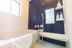 Une salle de bain avec une baignoire, une douche et un lavabo. Il y a deux bouteilles de shampoing sur une étagère.
