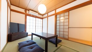 Ein traditioneller japanischer Raum mit Tatami-Böden, einem niedrigen Tisch, Kissen, Schiebetüren und einem Fernseher.