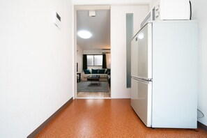 Ein Flur, der in ein Wohnzimmer führt, mit einem weißen Kühlschrank und einer Mikrowelle darauf.