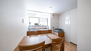 A modern kitchen with wooden cabinets, a dining table, and chairs. - TWS Morinomiya (Osaka)