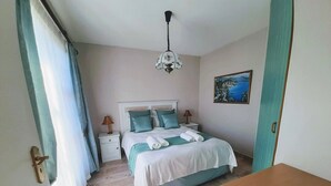 A bedroom with a bed, two bedside tables, a ceiling fan, and a painting on the wall. - Silverdunes Holiday Accommodation (Betty's Bay)