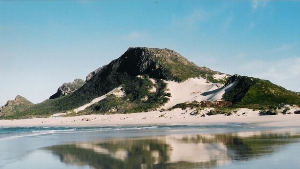 A beach with a mountain in the background and a clear reflection on the water. - Silverdunes Holiday Accommodation (Betty's Bay)