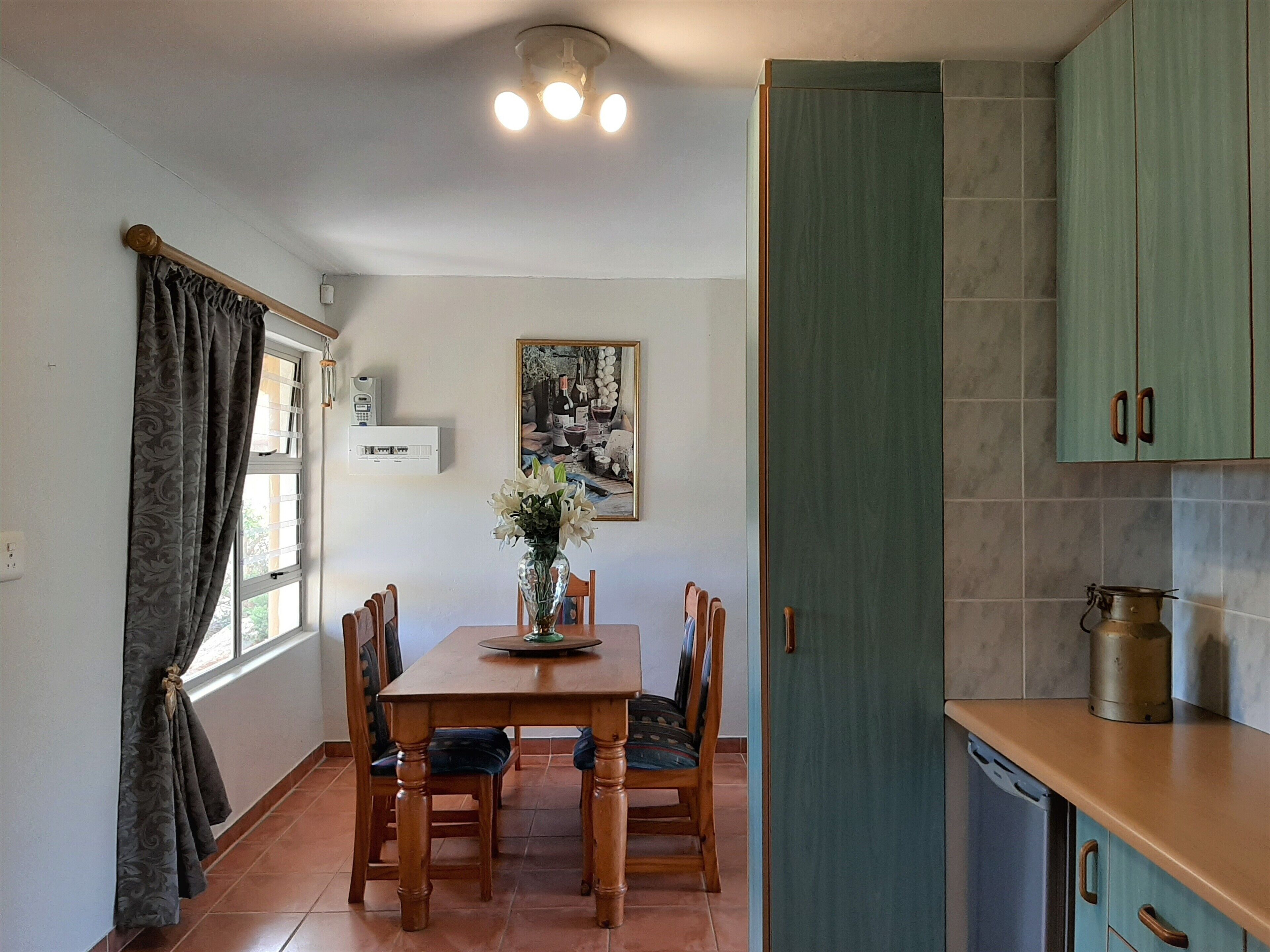 A dining area with a wooden table, chairs, a vase of flowers, and a painting on the wall.