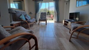 A spacious living room with wicker furniture, a television, and a view of the outdoors. - Silverdunes Holiday Accommodation (Betty's Bay)