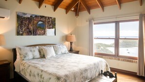 Un dormitorio con una cama grande, vigas de madera en el techo, una ventana con vistas al mar y un cuadro en la pared.