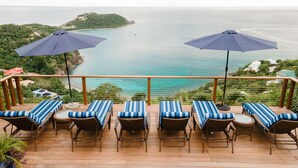 Una terraza con seis sillas de descanso y dos sombrillas, con vista al mar.
