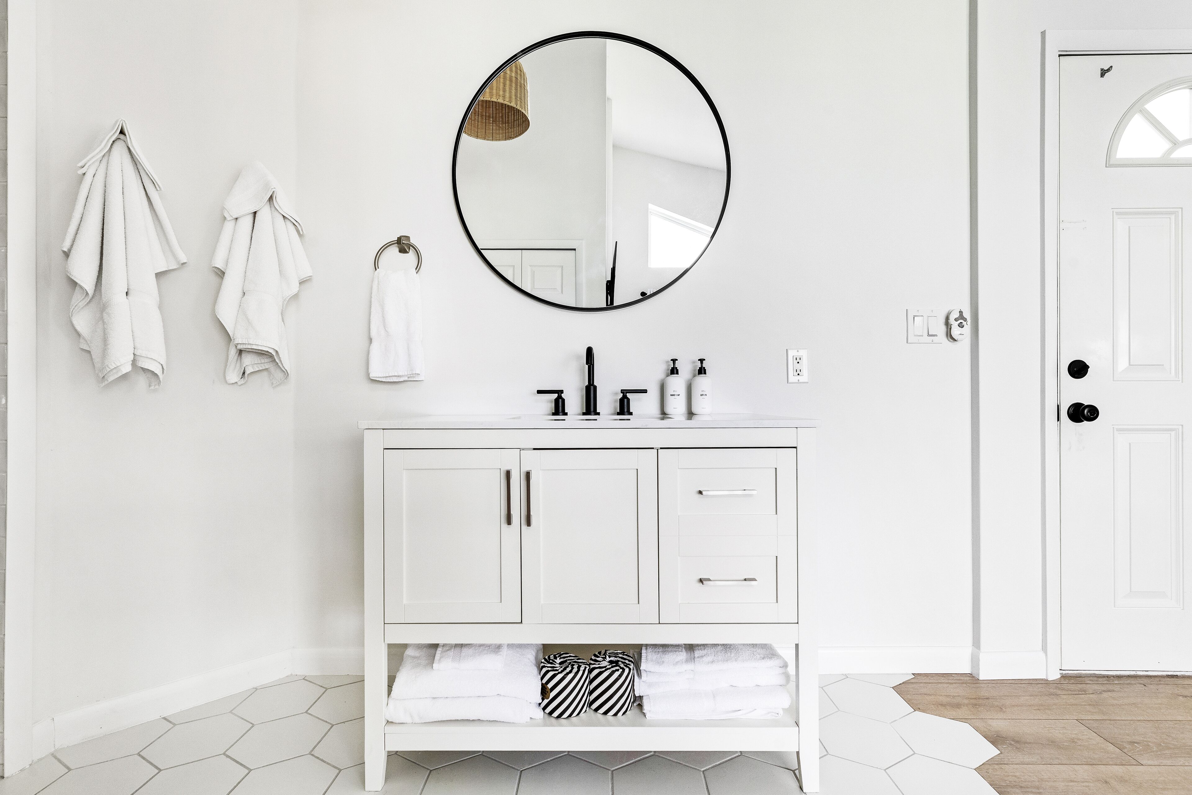 Un baño blanco con un espejo redondo, armarios blancos y una puerta blanca.