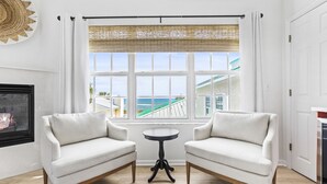 A room with a white sofa set, a small round table, and a view of a building and ocean through large windows. - Island Cottage Inn - Adults Only (Flagler Beach)
