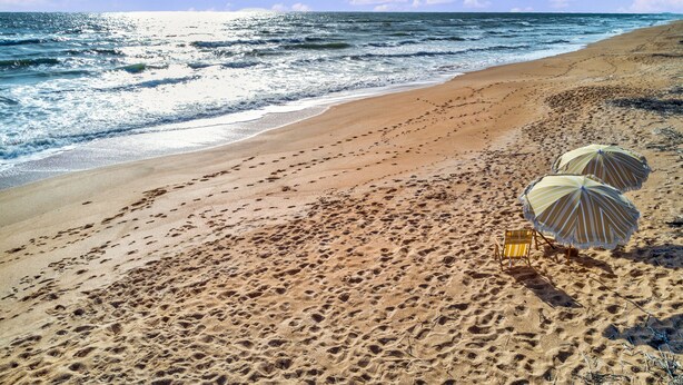 A beach with footprints leading to two beach umbrellas. - Island Cottage Inn - Adults Only (Flagler Beach)