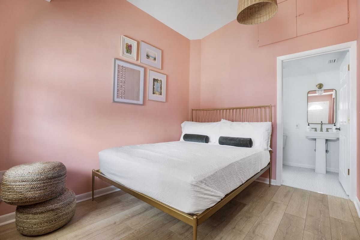 Ein Schlafzimmer mit einem Bett, einem Nachttisch, einem Wandspiegel und einer Tür zu einem Badezimmer.