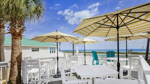 An outdoor seating area with white tables and chairs, yellow-striped umbrellas, and a view of the beach. - Island Cottage Inn - Adults Only (Flagler Beach)