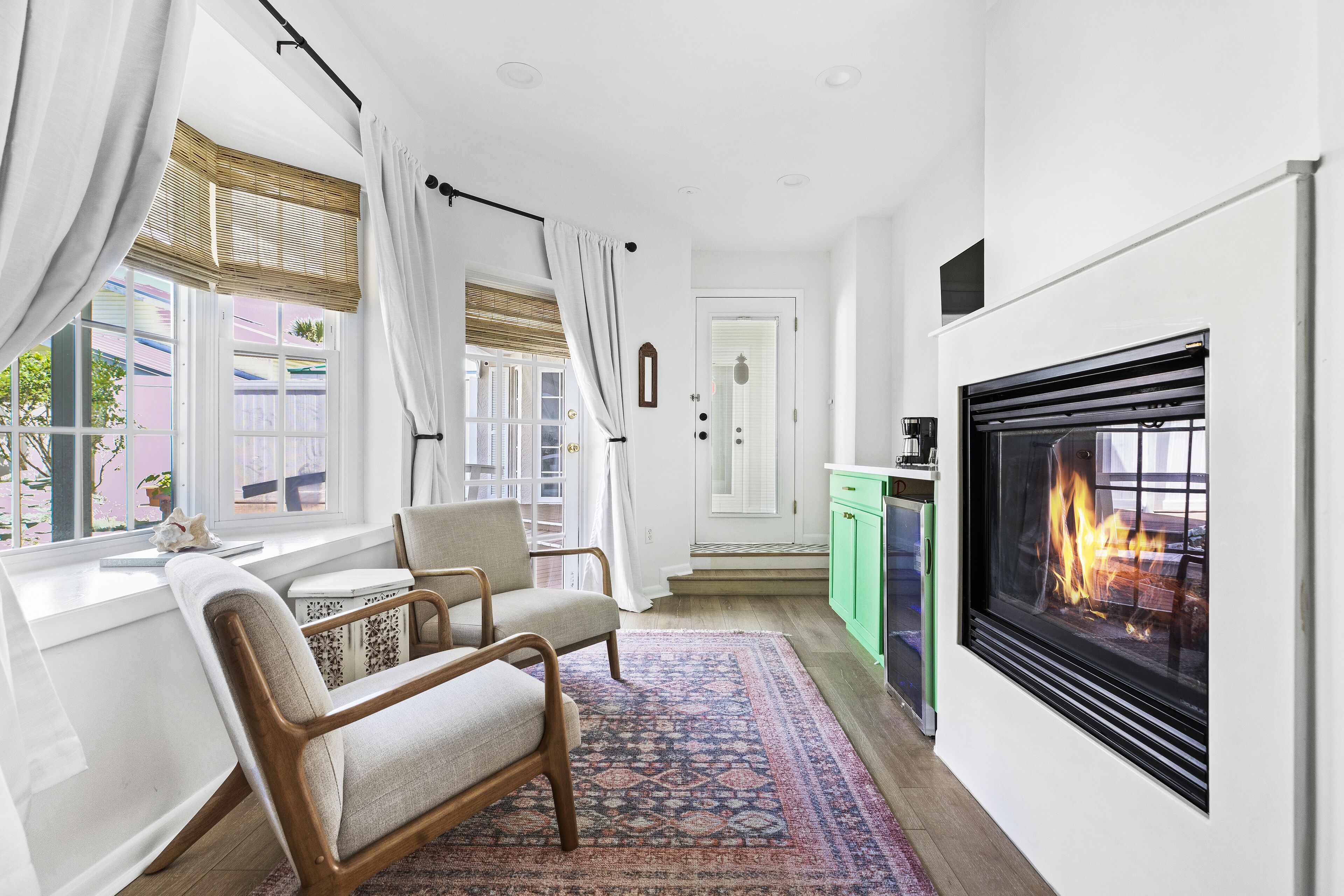 Una sala de estar con chimenea, una ventana con cortinas blancas y una alfombra estampada.