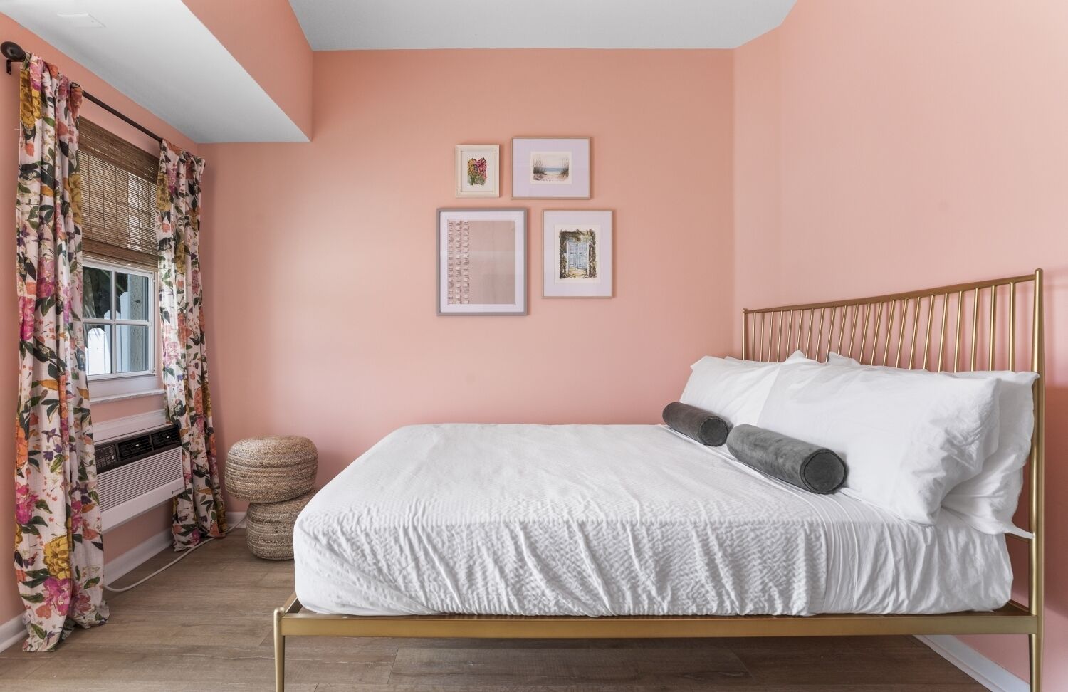 Ein Schlafzimmer mit einem Bett, einem Fenster mit blumigen Vorhängen und drei gerahmten Bildern an der Wand.