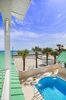A pool area with a view of the beach, palm trees, and a clear sky.