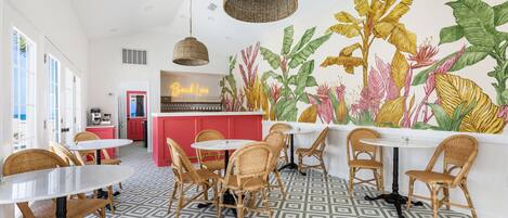 A restaurant with wicker chairs, white tables, and a mural of tropical plants.