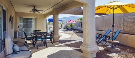 An outdoor patio with a covered seating area, including a table and chairs, and a yellow umbrella providing shade.