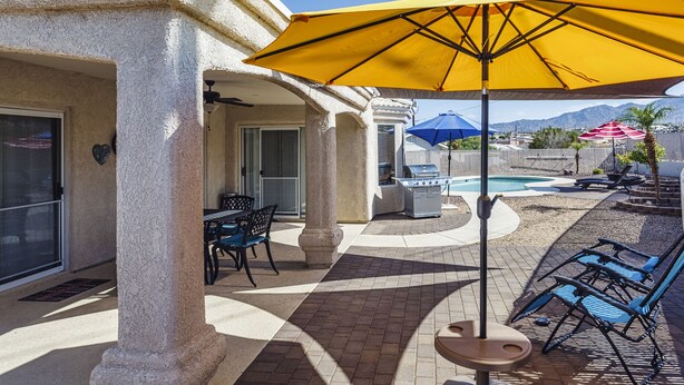 Un'area patio con un ombrellone giallo, mobili da esterno, un barbecue e una piscina.