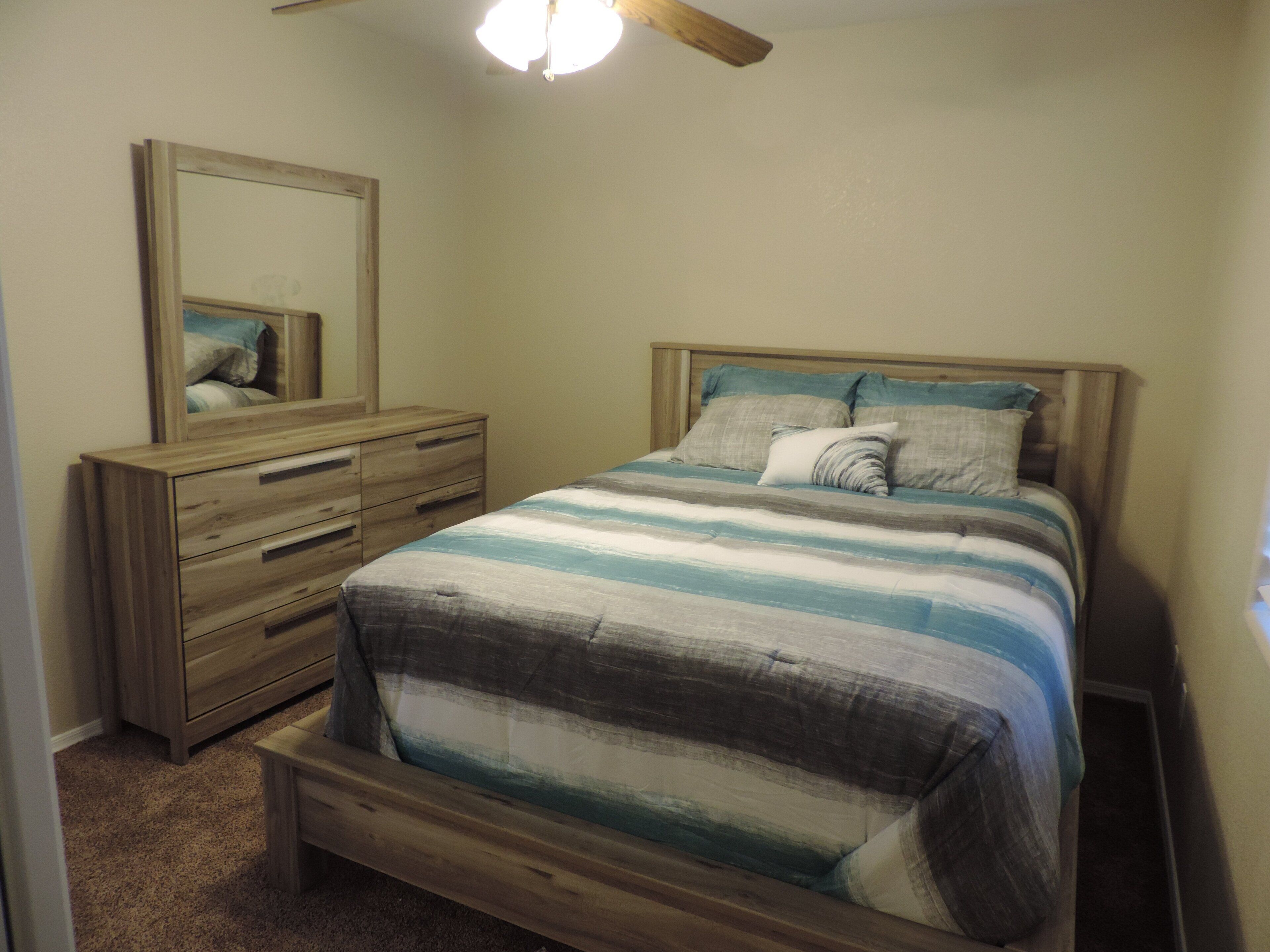 Een slaapkamer met een houten bedframe, een nachtkastje, een dressoir en een plafondventilator.