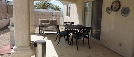 A covered patio area with a table and chairs, a ceiling fan, and a trash can.