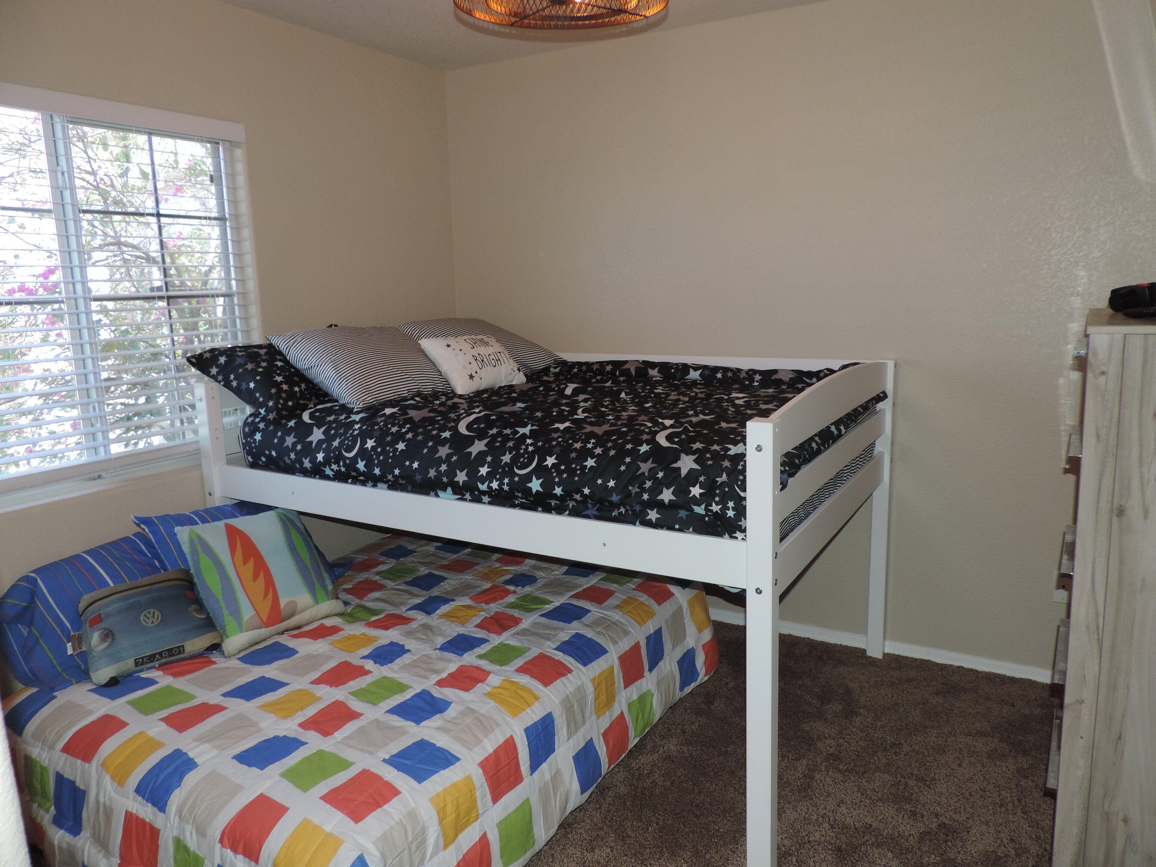 A bunk bed with a star-patterned top sheet and a colorful quilted bottom bed.