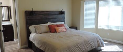 A bedroom with a large bed, a dark headboard, and a window with blinds.