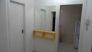 Un corridoio con pareti bianche, pavimento piastrellato e un mobile giallo contenitore.