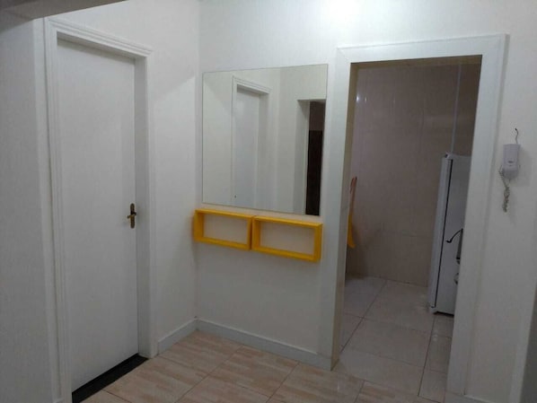 A hallway with white walls, a tiled floor, and a yellow shelf unit. - Apartment in Gonzaguinha 100 meters from the beach (São Vicente)