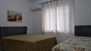 Una stanza con due letti, uno con una coperta a motivi e l'altro con una fantasia floreale. C'è un quadro appeso al muro e un condizionatore sopra la finestra.