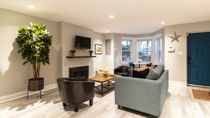 A modern living room with a grey sofa, black armchairs, a wooden coffee table, and a large potted plant. - Lovely Shaw Apartment - Sleeps 4, WALK to White House (Washington)
