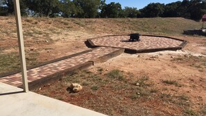 A paved outdoor area with a circular brick pattern, a concrete pathway, and a stone feature. - Willow Knoll 2 Texas (Fredericksburg)