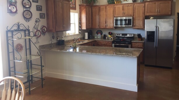 A kitchen with wooden cabinets, a stainless steel refrigerator, a microwave, and a granite countertop. - Willow Knoll 2 Texas (Fredericksburg)