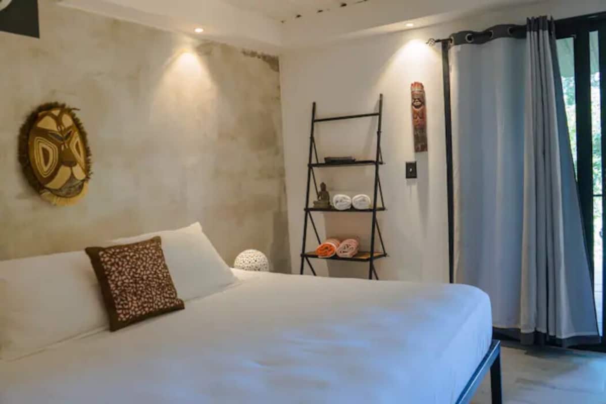 Une chambre avec un grand lit, une étagère fixée au mur où sont rangées des serviettes, et un masque décoratif accroché au mur.