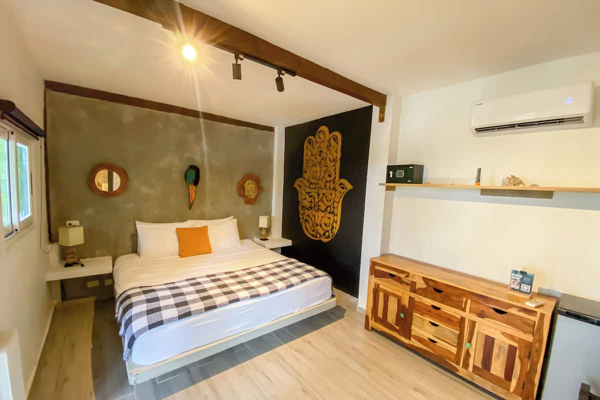 Une chambre à coucher comprenant un lit, des tables de chevet, une commode en bois, un climatiseur et des éléments décoratifs muraux.