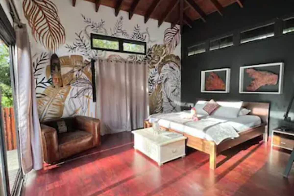 Une chambre avec un plafond en bois, un lit, une table de chevet, un canapé et une fenêtre avec des rideaux.