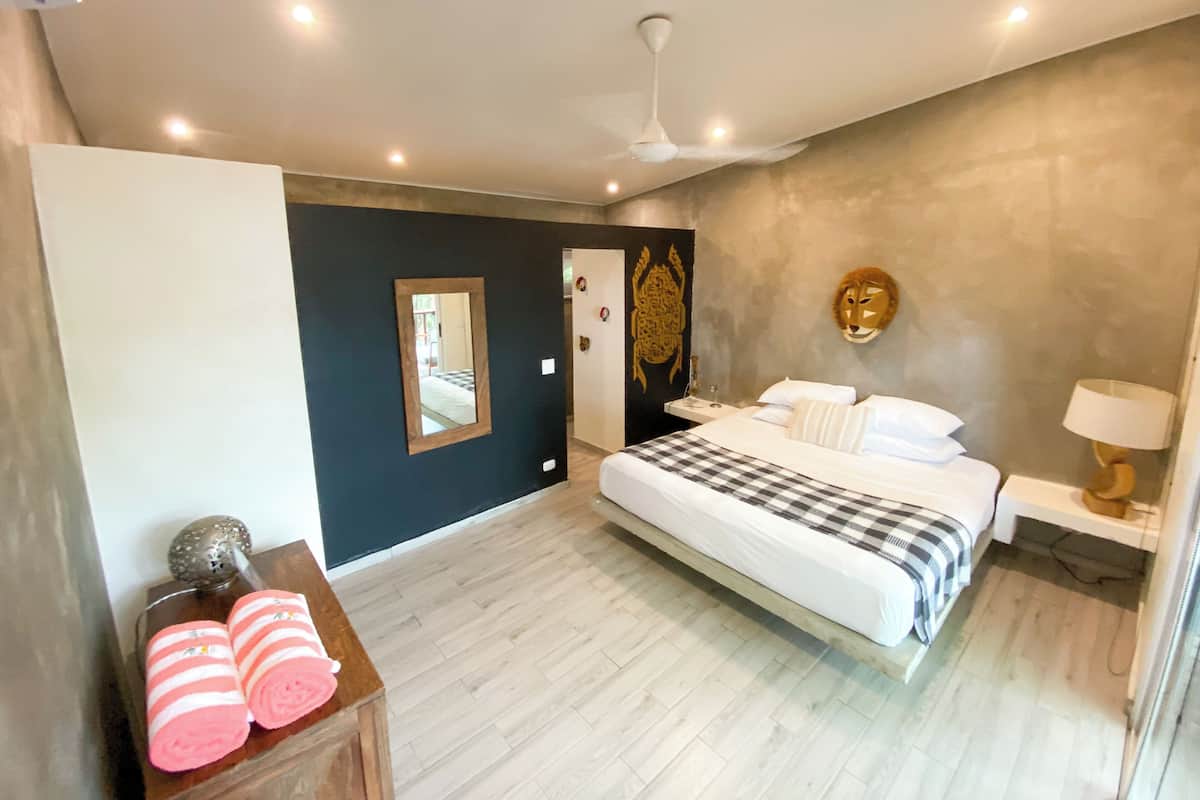 Une chambre à coucher moderne avec un grand lit, une table de chevet, un miroir et une lampe fixée au mur.