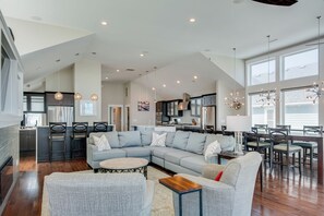 A spacious living area with a large L-shaped sectional sofa, a dining table with chairs, and a kitchen in the background. - Go Your Own Wave: Oceanfront, Pool, Spa, Elevator (Nags Head)