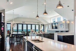 A modern kitchen with a large island, stainless steel appliances, and pendant lighting. - Go Your Own Wave: Oceanfront, Pool, Spa, Elevator (Nags Head)