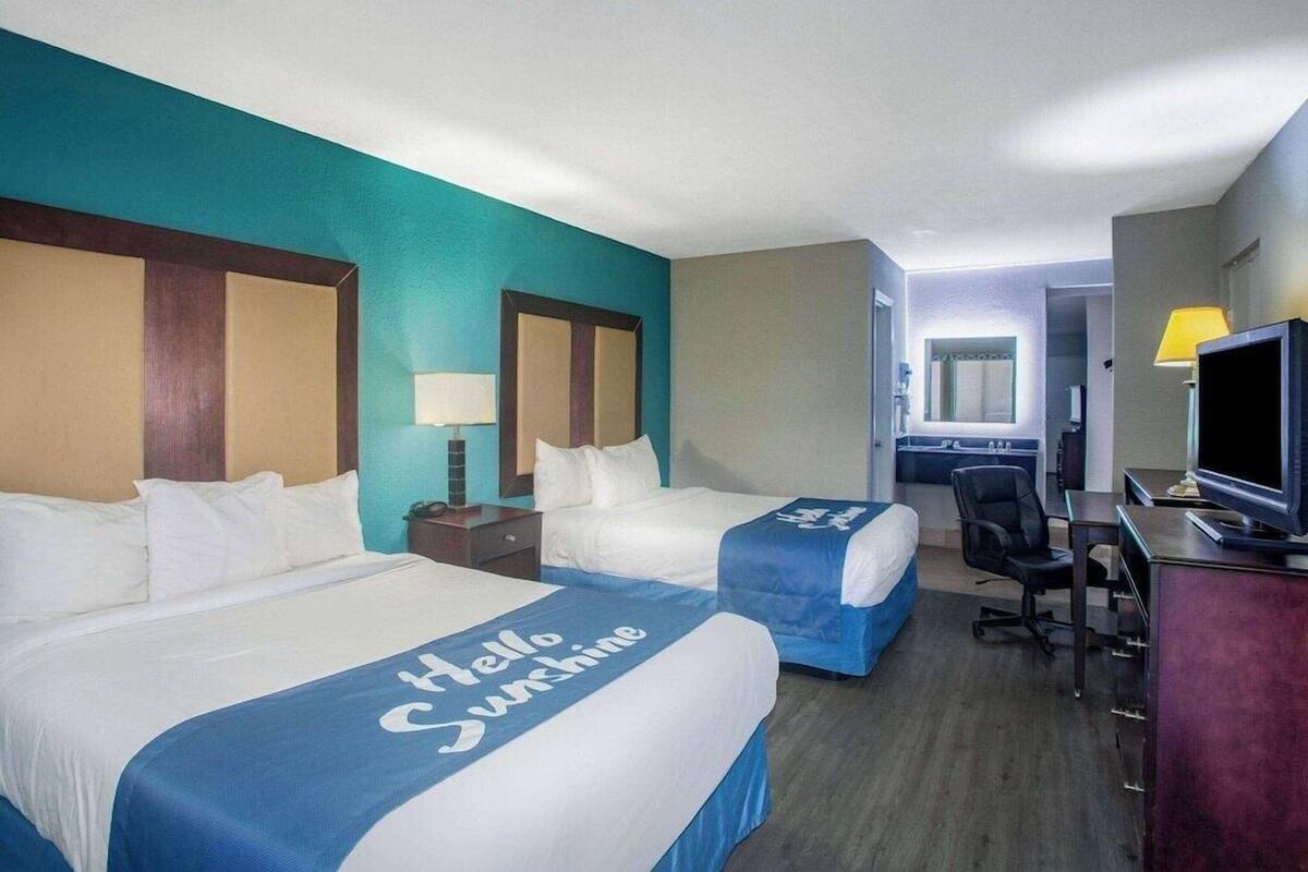 A hotel room with two beds, a desk, a chair, a television, and a bathroom visible in the background.