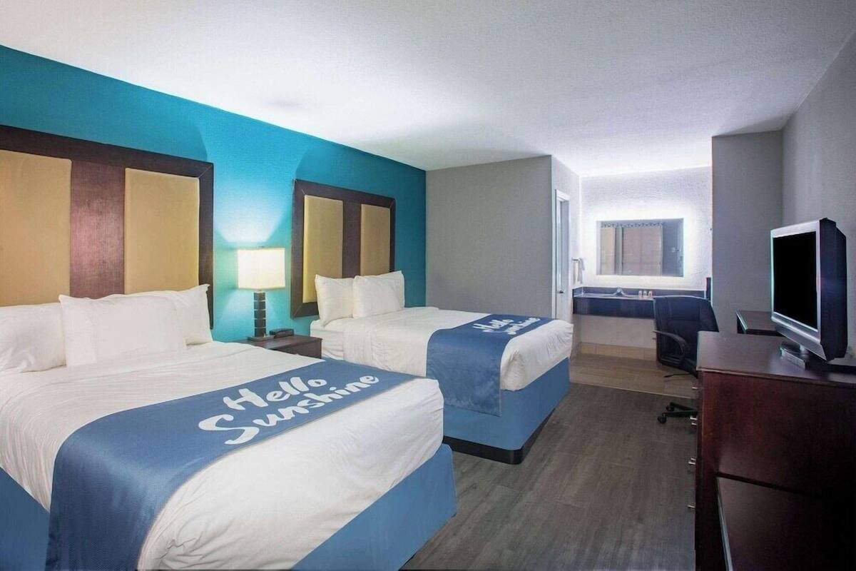 A hotel room with two beds, a desk, a television, and a window.