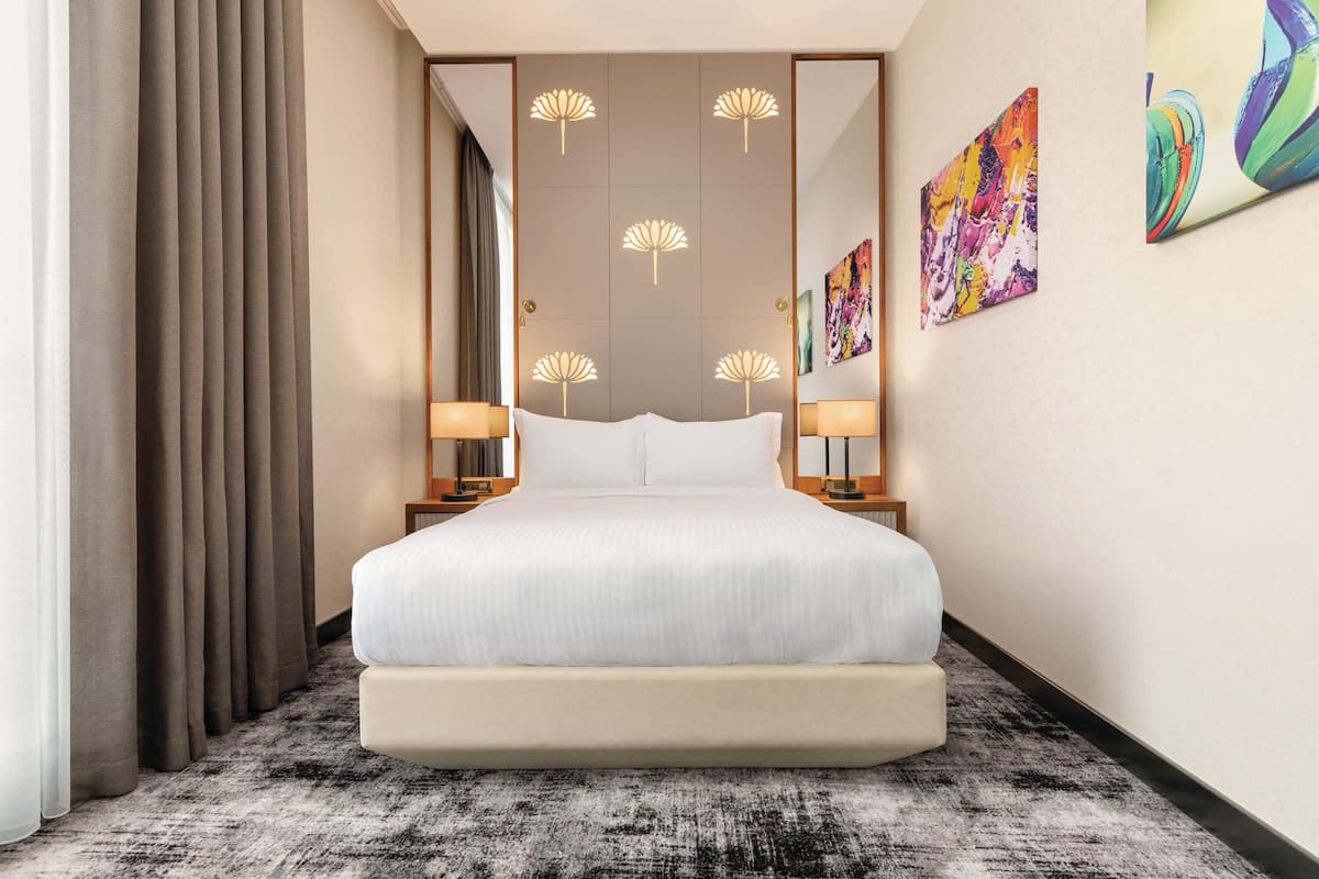 A modern hotel room with a large bed, a mirror, and two wall-mounted lamps.